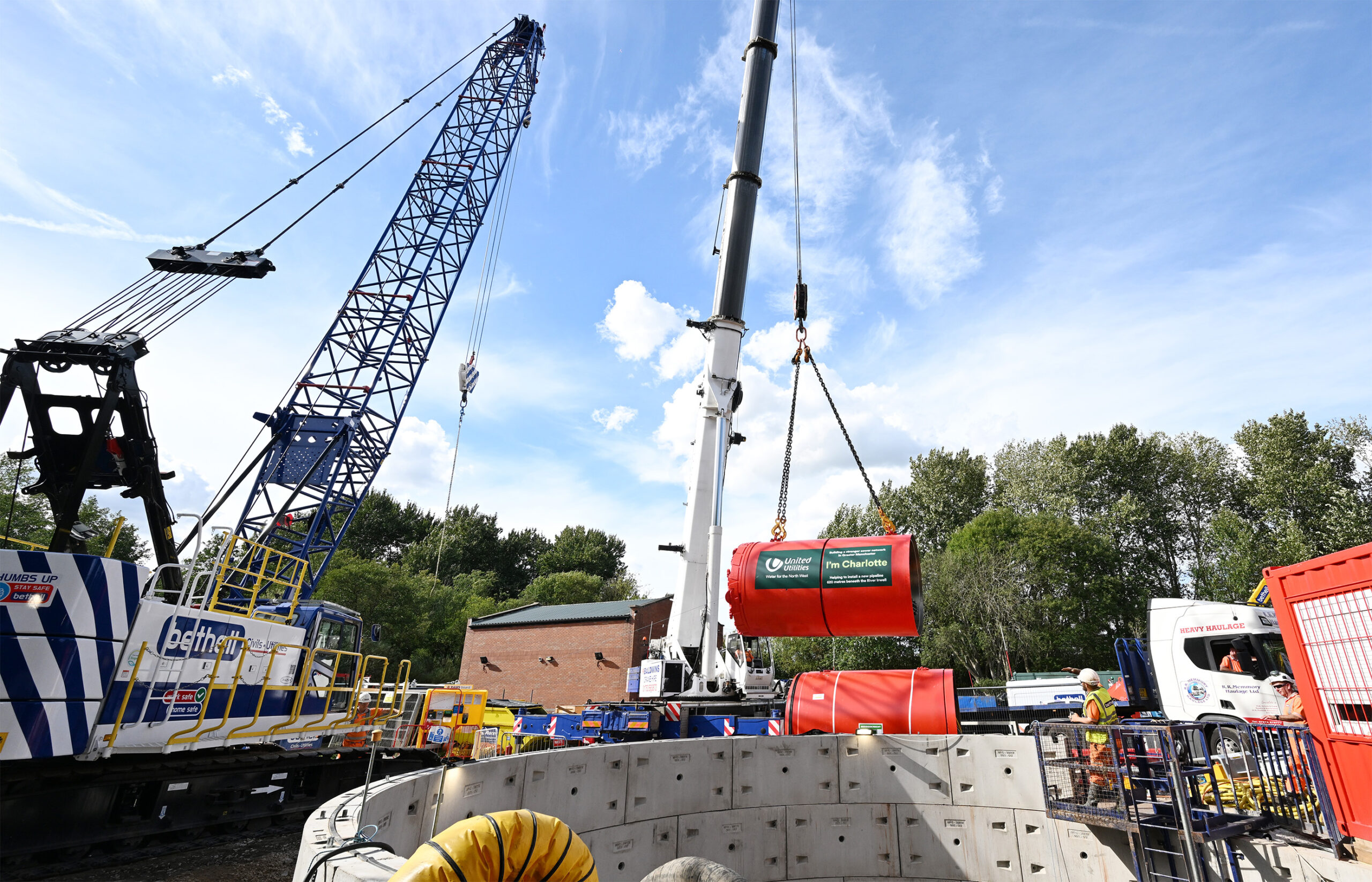 Crane lowering a red tunnel boring machine into a shaft