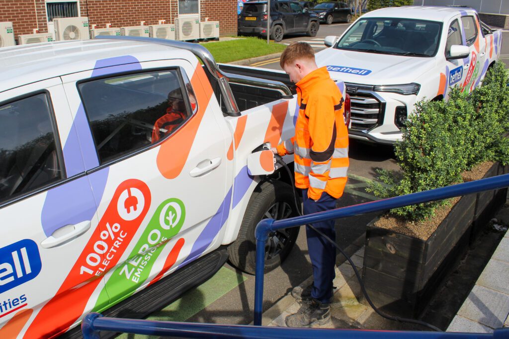 An operative in orange PPE plugging a charger into an electric pick up truck