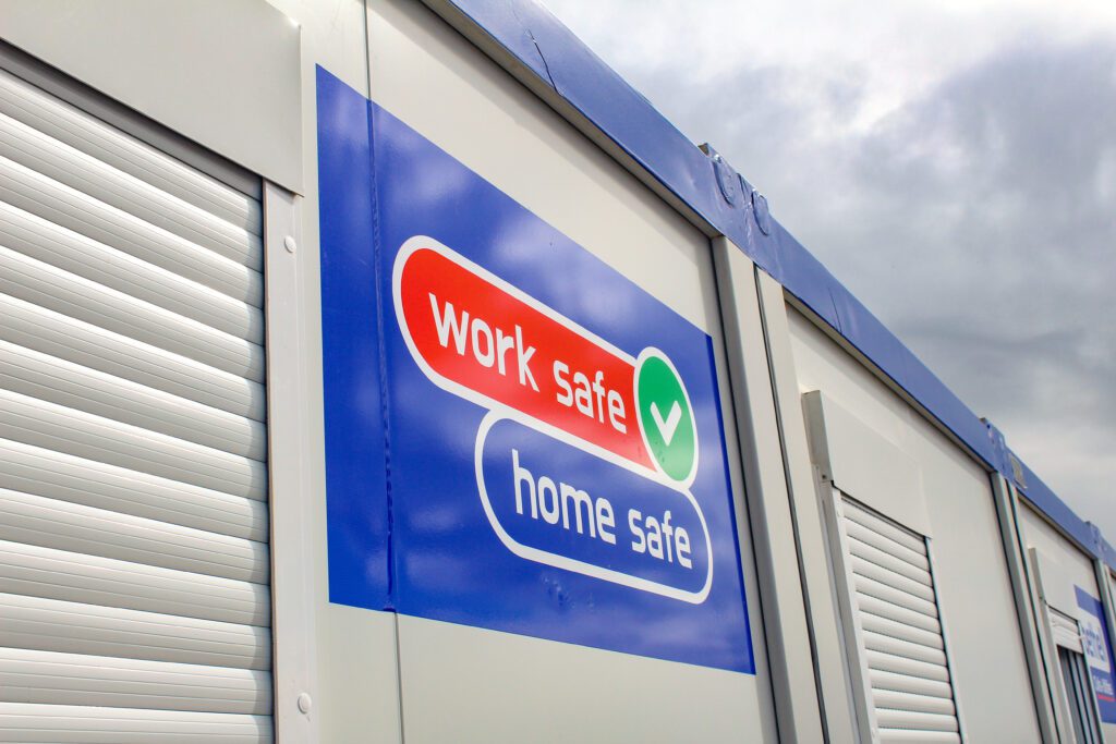 A close up of a sign attached to an office building, which reads "Work Safe Home Safe"