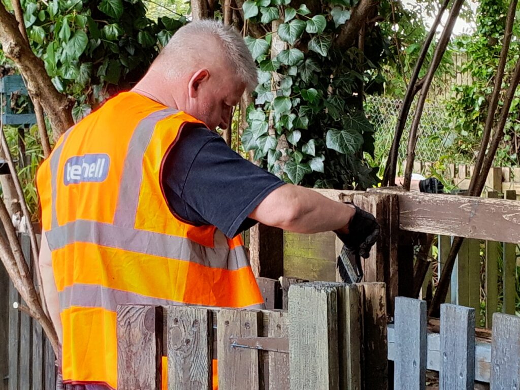 A volunteer in orange PPE painting a fence