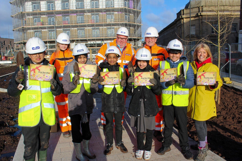 A group of operatives and schoolchildren in yellow PPE holding seed boxes