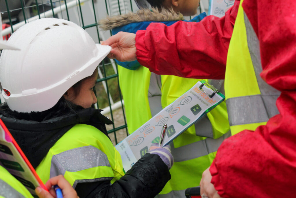 A school pupil in yellow PPE holding a clipboard