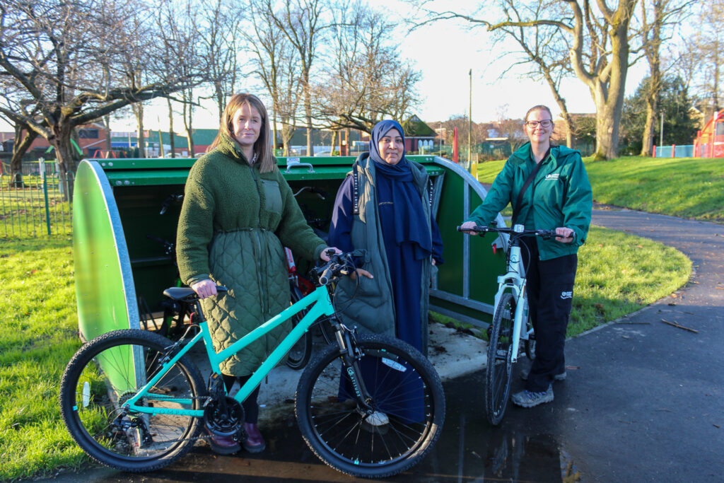 A group of people with bikes outside an outdoors bike shed in a public park