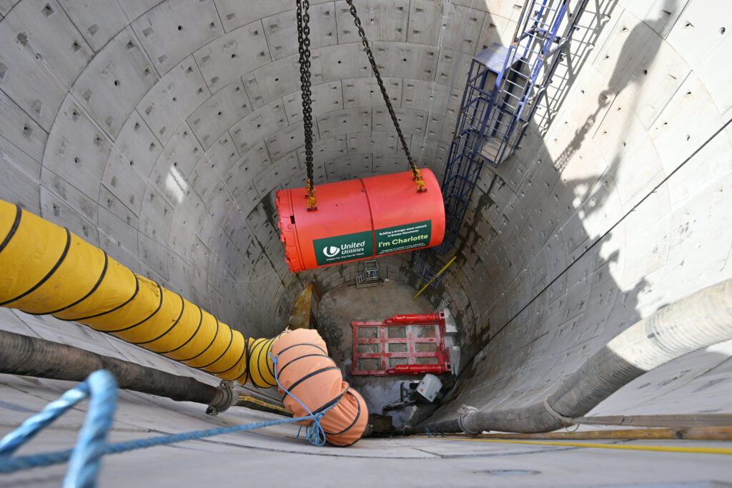 A red tunnel boring machine named "Charlotte" being lifted down a shaft